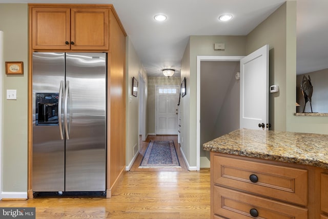 kitchen with light stone counters, kitchen peninsula, stainless steel fridge with ice dispenser, and light hardwood / wood-style flooring