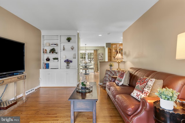 living room with a notable chandelier, built in shelves, and wood-type flooring