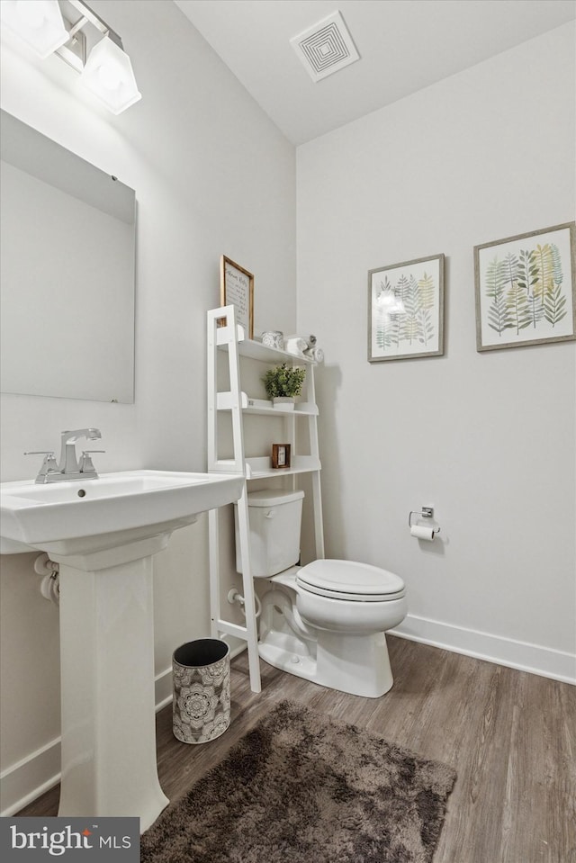 half bathroom with visible vents, baseboards, toilet, wood finished floors, and a sink