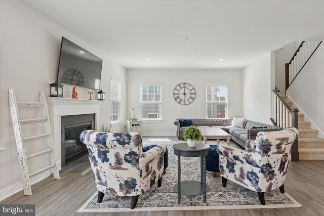 living area with baseboards, stairway, recessed lighting, wood finished floors, and a glass covered fireplace