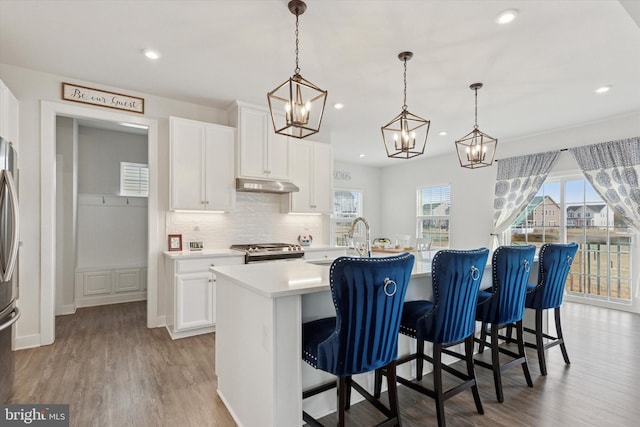 kitchen with wood finished floors, a sink, under cabinet range hood, stainless steel gas range oven, and a chandelier