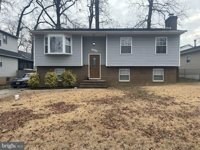 split foyer home featuring entry steps, a chimney, and brick siding