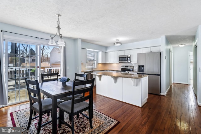 kitchen with white cabinets, dark wood finished floors, appliances with stainless steel finishes, a center island, and a sink