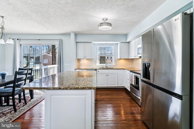 kitchen featuring dark stone counters, dark wood-style flooring, stainless steel appliances, white cabinetry, and backsplash