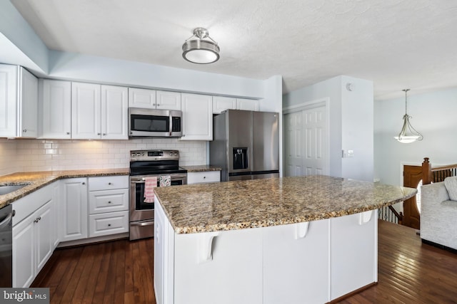 kitchen featuring stainless steel appliances, dark wood finished floors, white cabinetry, tasteful backsplash, and a kitchen bar