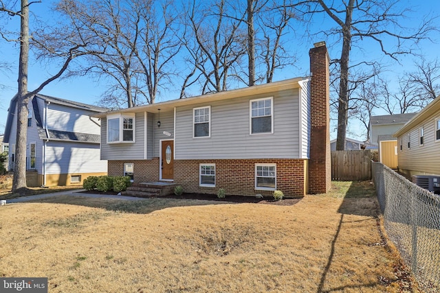 raised ranch with central AC, brick siding, a chimney, and fence