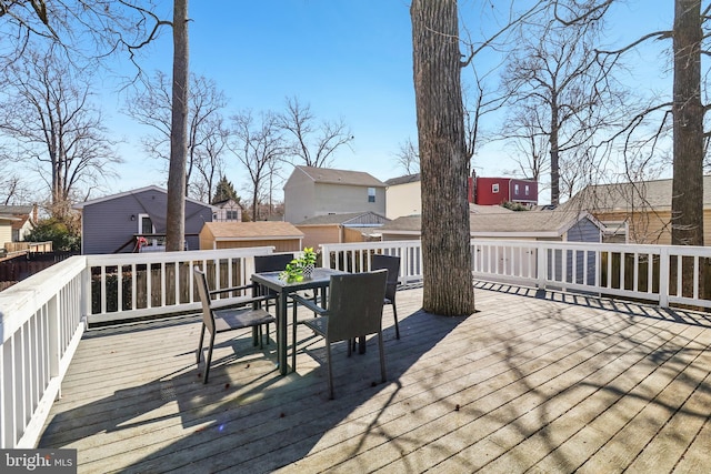 wooden terrace featuring a residential view, outdoor dining area, and an outbuilding