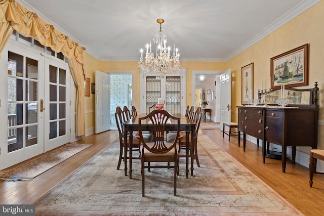 dining area featuring a notable chandelier, crown molding, french doors, and light wood-type flooring