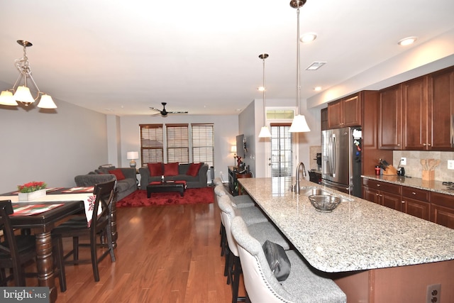 kitchen featuring sink, dark wood-type flooring, a breakfast bar area, hanging light fixtures, and stainless steel refrigerator with ice dispenser