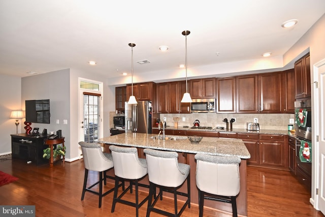 kitchen featuring appliances with stainless steel finishes, decorative light fixtures, an island with sink, sink, and backsplash