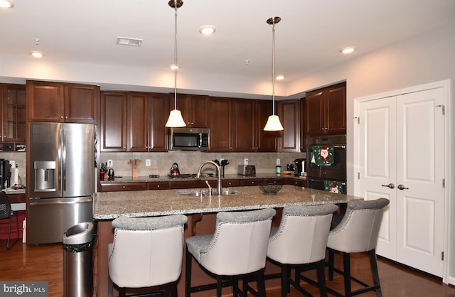 kitchen with pendant lighting, sink, stainless steel appliances, light stone countertops, and a center island with sink