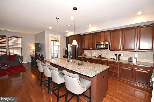 kitchen with stainless steel appliances, a center island with sink, a breakfast bar, and pendant lighting