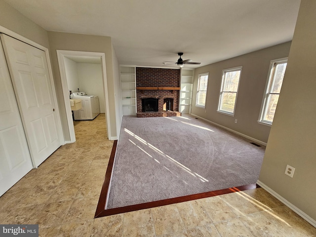 unfurnished living room with a brick fireplace, built in shelves, independent washer and dryer, and ceiling fan