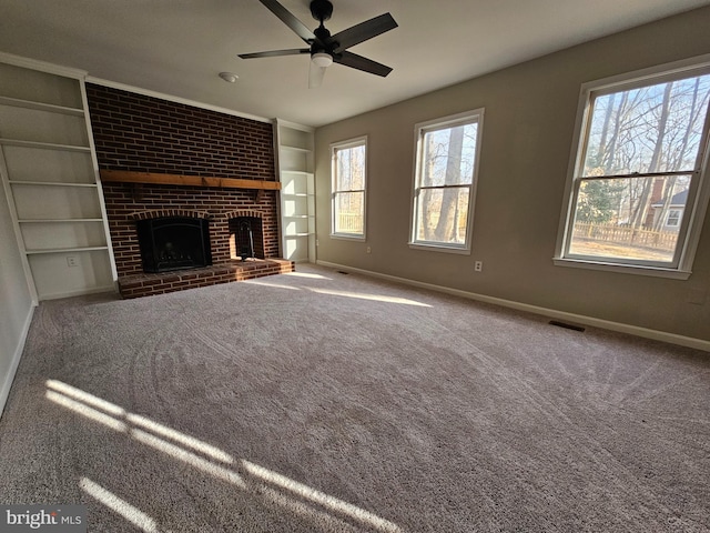 unfurnished living room featuring a brick fireplace, built in shelves, ceiling fan, and carpet