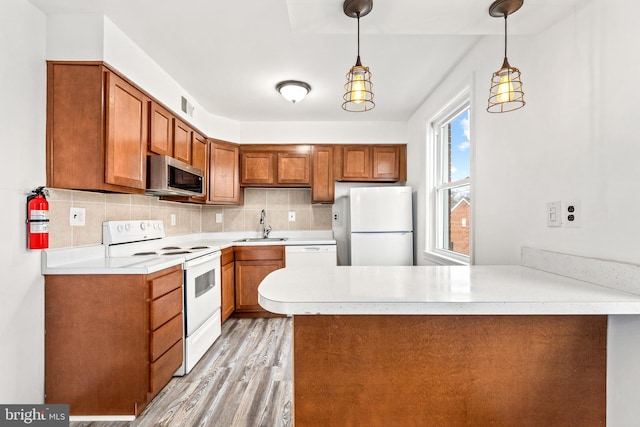 kitchen featuring sink, white appliances, decorative light fixtures, and kitchen peninsula