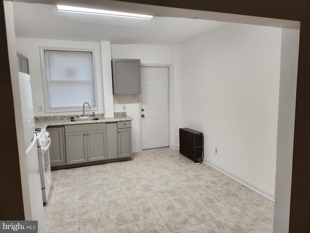 kitchen featuring sink, gray cabinetry, radiator heating unit, light stone countertops, and white gas range oven