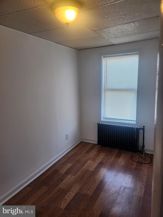 spare room featuring dark hardwood / wood-style flooring, radiator, and a paneled ceiling