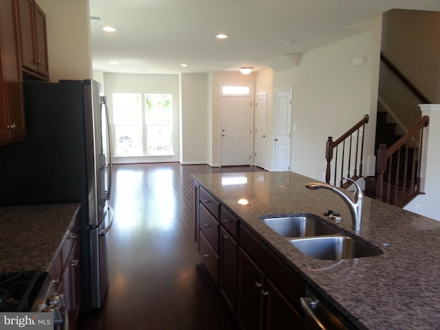 kitchen with appliances with stainless steel finishes, dark hardwood / wood-style floors, sink, and dark stone countertops