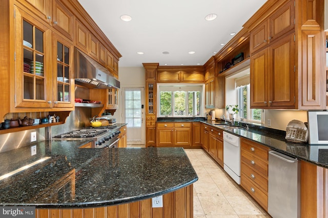 kitchen featuring dark stone counters, dishwasher, glass insert cabinets, ventilation hood, and stainless steel range with gas stovetop