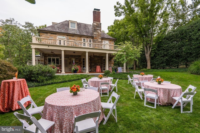 rear view of house featuring a ceiling fan, a patio, stone siding, outdoor dining area, and a yard