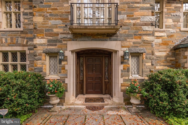 view of exterior entry with a balcony and stone siding