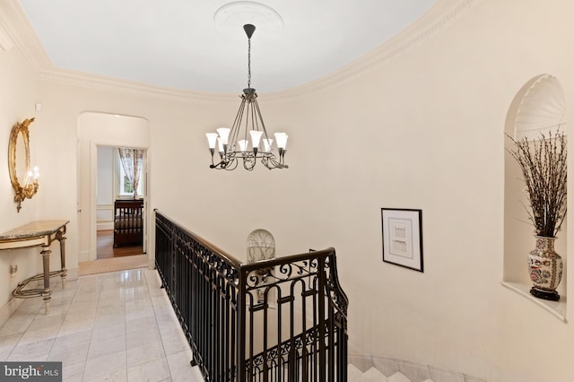 hall featuring ornamental molding, a chandelier, arched walkways, and an upstairs landing