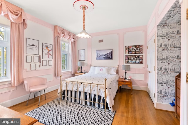 bedroom with multiple windows, visible vents, baseboards, and wood finished floors