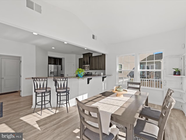 dining area with high vaulted ceiling and light hardwood / wood-style flooring