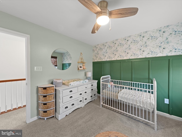 bedroom featuring a nursery area, light carpet, and ceiling fan