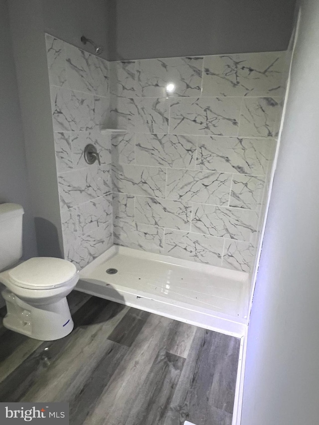 bathroom with wood-type flooring, tiled shower, and toilet