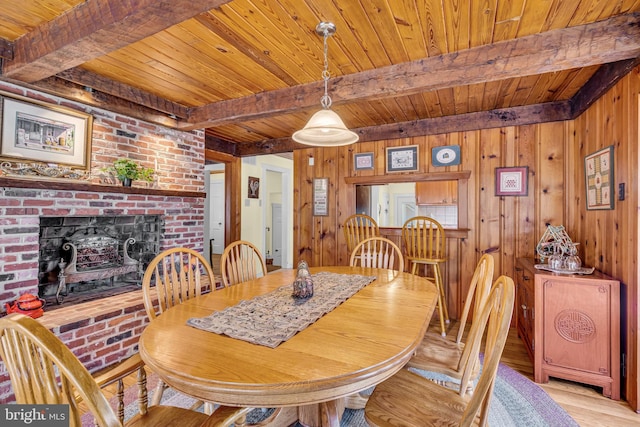 dining space featuring beamed ceiling, wooden walls, a brick fireplace, and wooden ceiling