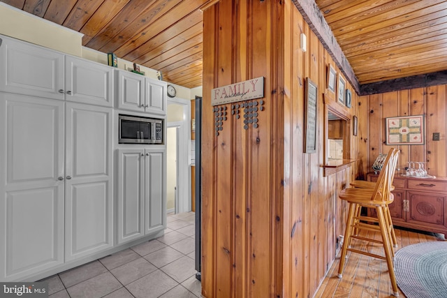 kitchen featuring stainless steel microwave, wood walls, white cabinets, light tile patterned floors, and wooden ceiling