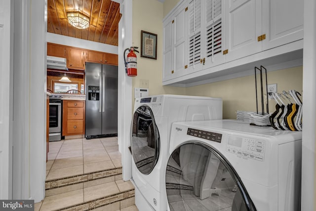 clothes washing area with light tile patterned floors, wood ceiling, cabinets, and washing machine and clothes dryer