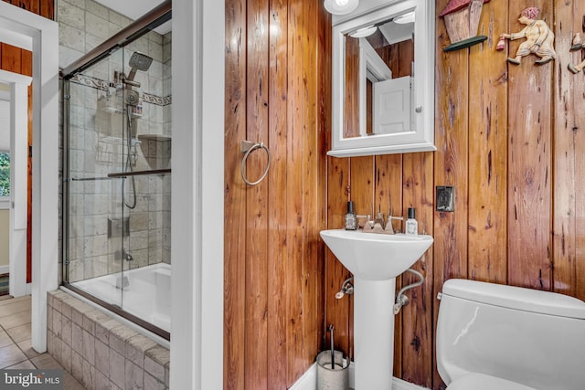 bathroom featuring wooden walls, tile patterned floors, toilet, and combined bath / shower with glass door