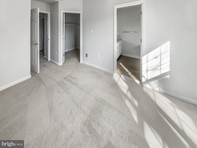 unfurnished bedroom featuring ensuite bath, a walk in closet, light colored carpet, and a closet