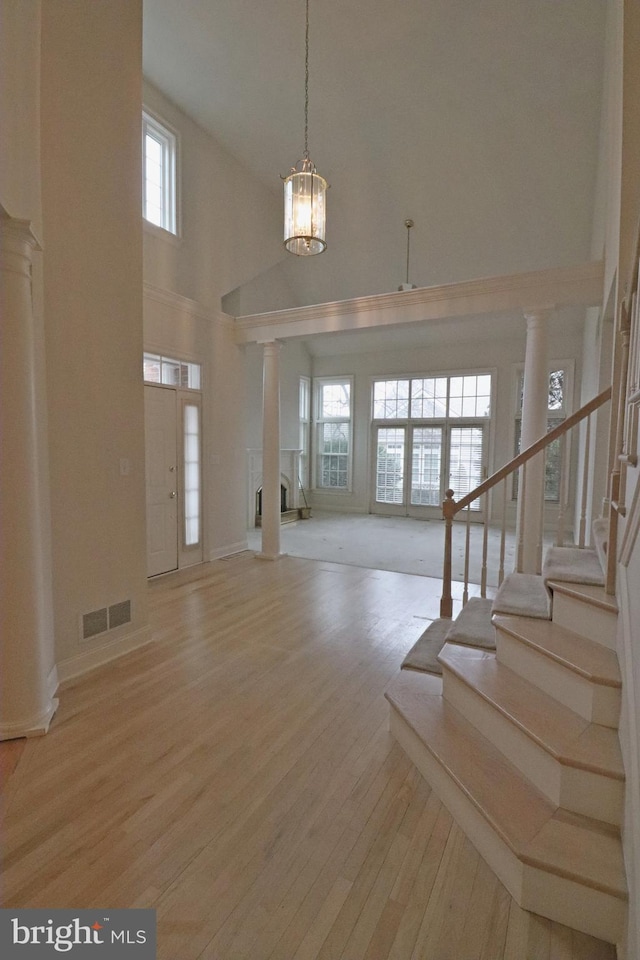 foyer with a towering ceiling, decorative columns, and light hardwood / wood-style flooring