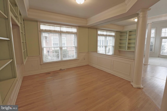 empty room featuring a tray ceiling, ornamental molding, light hardwood / wood-style floors, and ornate columns