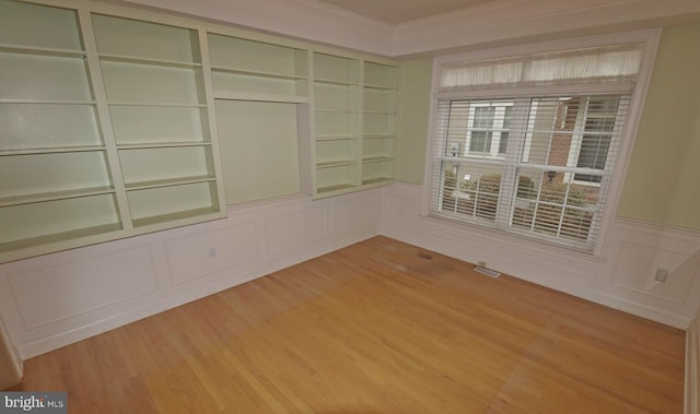 spare room featuring crown molding, built in features, and light hardwood / wood-style floors