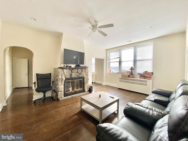 living room featuring radiator, a stone fireplace, dark hardwood / wood-style floors, and ceiling fan