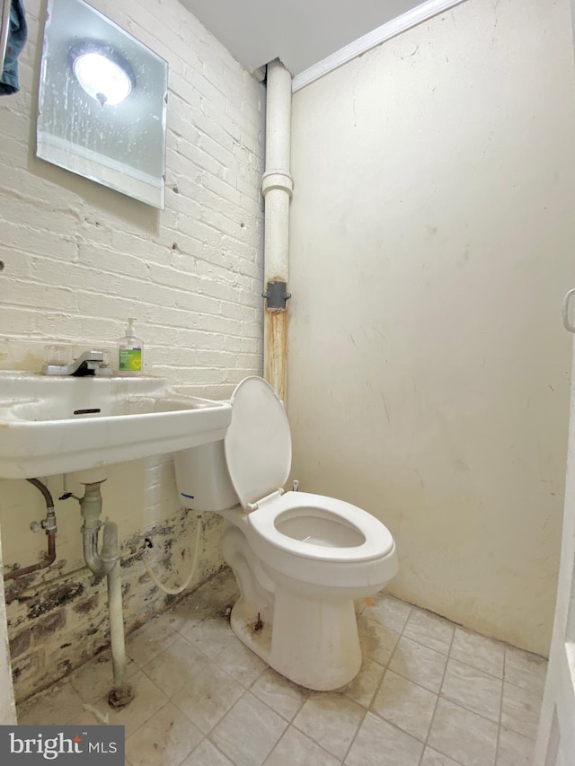 bathroom with brick wall, toilet, and tile patterned flooring