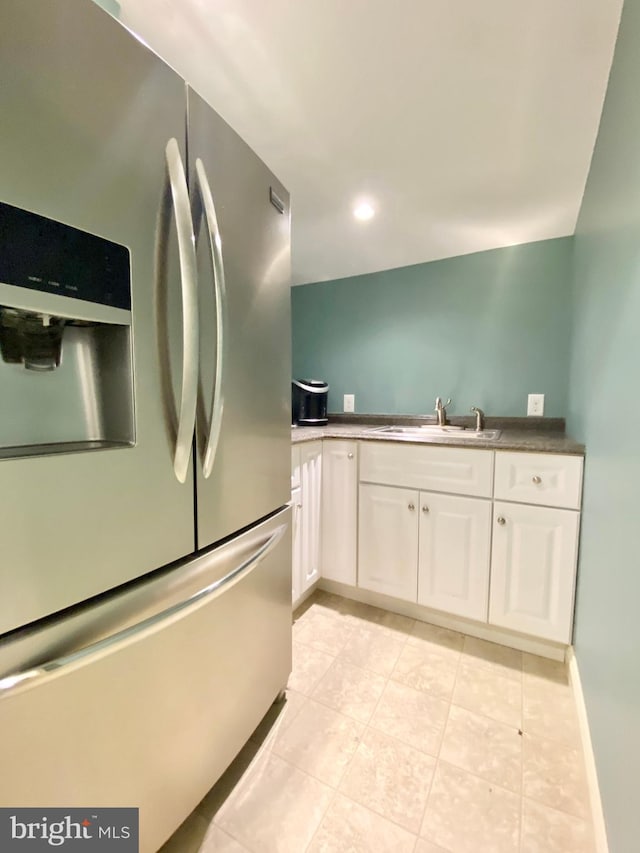 kitchen featuring white cabinetry, stainless steel fridge, light tile patterned flooring, and sink