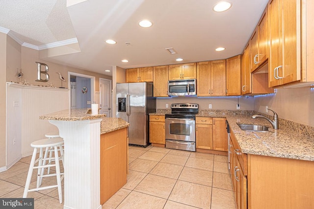 kitchen featuring a kitchen bar, sink, a center island, stainless steel appliances, and light stone countertops