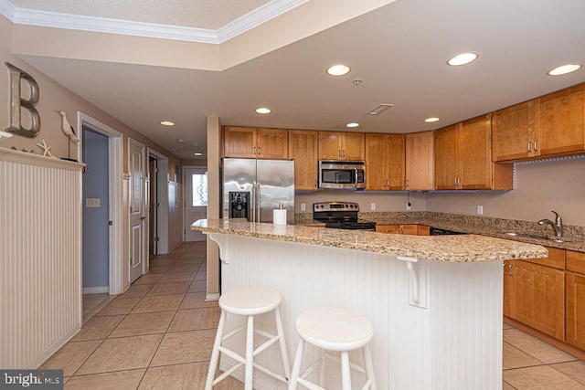 kitchen featuring a kitchen island, appliances with stainless steel finishes, a breakfast bar, sink, and light stone counters