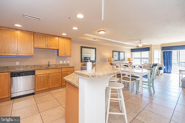 kitchen with light tile patterned floors, a breakfast bar, dishwasher, light stone countertops, and a kitchen island