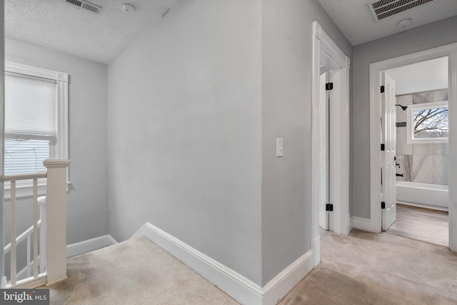 hallway with light colored carpet and a textured ceiling