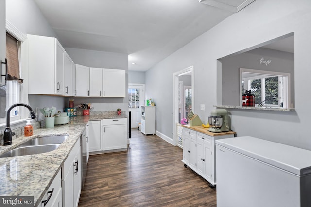 kitchen with a wealth of natural light, white cabinetry, sink, dark hardwood / wood-style flooring, and light stone countertops