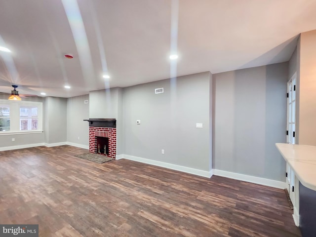 unfurnished living room with a brick fireplace, dark hardwood / wood-style floors, and ceiling fan