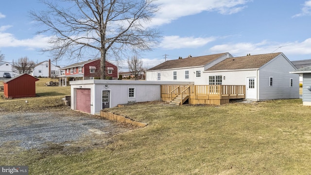 back of house featuring a garage, a wooden deck, a yard, and an outbuilding