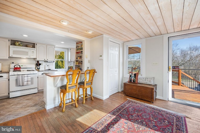 kitchen featuring white appliances, light hardwood / wood-style flooring, white cabinets, and a kitchen bar