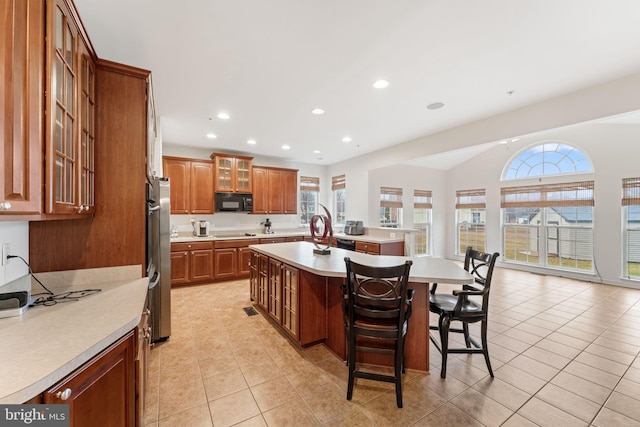 kitchen featuring light tile patterned flooring, refrigerator, an island with sink, lofted ceiling, and a kitchen breakfast bar